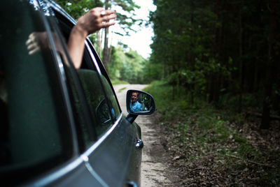 Cropped hand of man waving from car on road