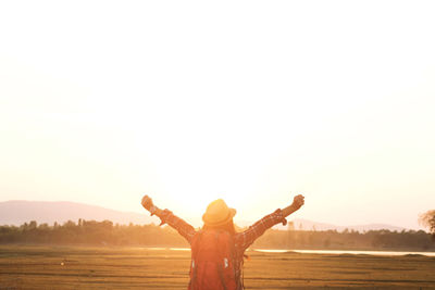 Rear view of woman with arms outstretched standing against sky