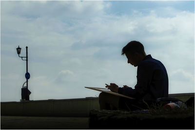 Side view of man using smart phone against sky