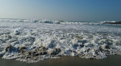 Waves rushing towards shore against clear sky