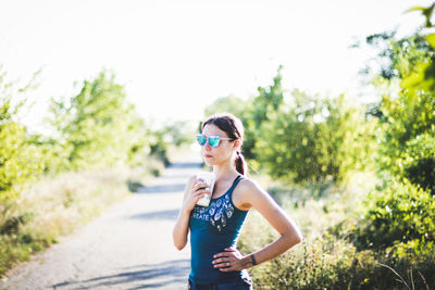 Woman wearing sunglasses while holding disposable cup on road