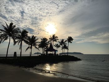 Silhouette palm trees by swimming pool against sky during sunset