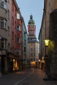 Illuminated street amidst buildings against sky at dusk