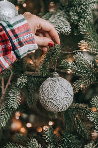 Female hand hanging silver bauble on christmas tree