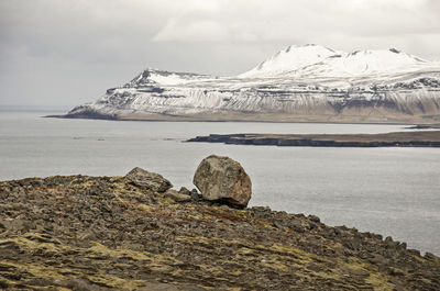 Large rock on a slope with gravel and moss and with snow-covered mountains in the background 