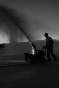 Side view of man using snowblower against sky