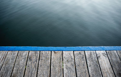 Edge of empty wooden dock against calm blue lake water.