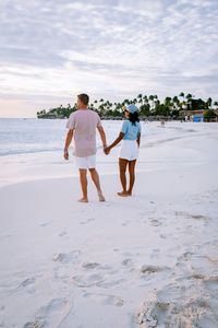 Rear view of friends standing on beach against sky