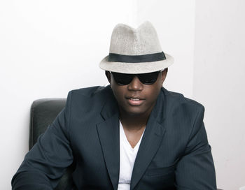 Young man sitting against white wall