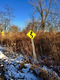 Road sign on snow covered field against sky