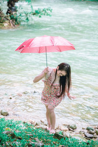 Full length of woman walking with umbrella on rock by river