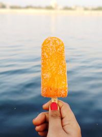 Cropped hand of woman holding flavored ice against lake