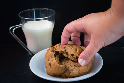 Cropped hand of woman holding cookie by milk glass