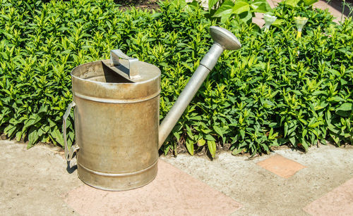 An old vintage metal watering can in the garden, outdoors, with a flower garden in the background