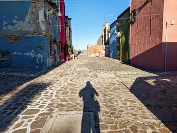 Shadow of man on footpath amidst buildings in city