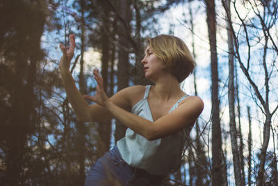 Low angle view of young woman dancing in forest