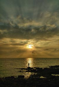 Silhouette person standing by sea against sky during sunset
