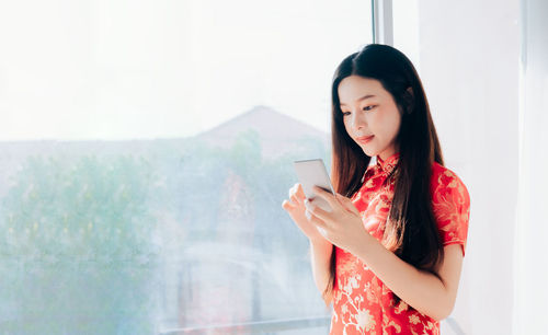 Young woman using phone while standing on wall