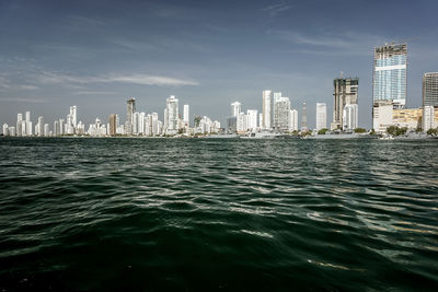 Sea by modern buildings in city against sky