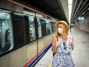 Woman wearing mask looking away while standing at railroad station platform