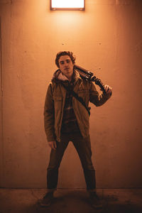 Portrait of young man holding tripod while standing against wall