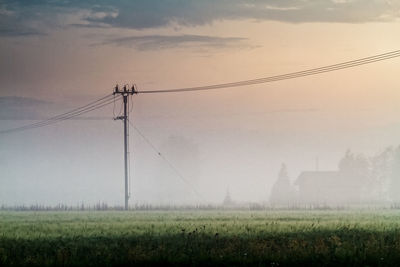 Electricity pylon on field against sky during foggy weather
