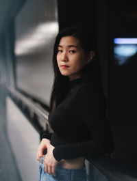 Portrait of young woman standing against window