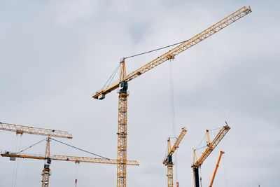 Low angle view of cranes at construction site against sky