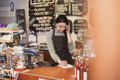 Owner talking on phone while writing on note pad at checkout counter in store