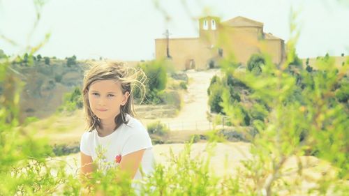 Portrait of girl sitting on field during sunny day