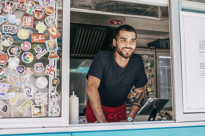 Smiling young male owner standing in food truck seen through window