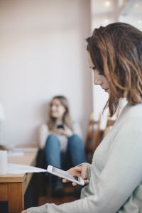 Side view of woman using mobile phone with female friend in background