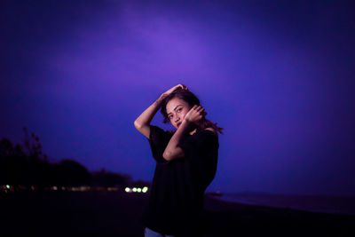 Portrait of woman standing at beach against sky at night
