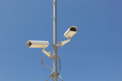 Low angle view of security camera against clear blue sky