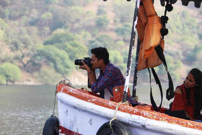 Man with woman photographing through camera while sitting in boat on lake