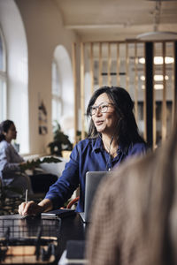 Smiling female business professional talking through wired headphones at coworking office