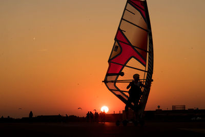 Silhouette man on surfboard against orange sky