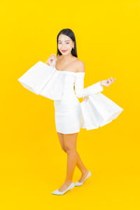 Full length portrait of woman standing against yellow background
