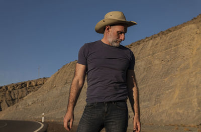 Adult man in cowboy on roadside on desert against mountain. almeria, spain