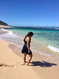 Side view of young woman standing at beach against blue sky