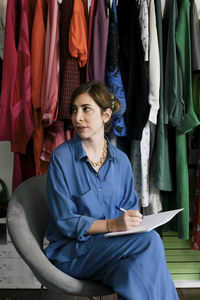 Female entrepreneur with book and pen looking away in boutique