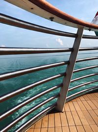 Wooden railing by sea against blue sky