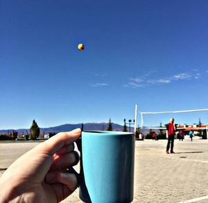 Cropped image of man holding drink against blue sky