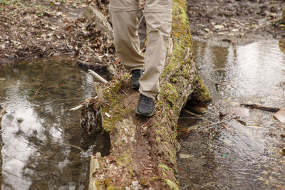 Bottom-half of a man crossing a creek on moss-covered log in nature