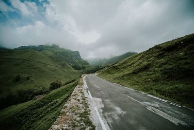 Road leading towards mountain against cloudy sky