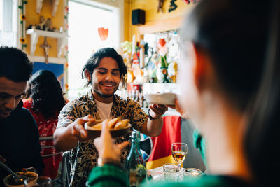 Smiling young man giving food to woman while sitting by friend at table in restaurant during brunch party