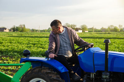 A farmer on a tractor monitors the operation of equipment for harvesting potatoes. farming farmland