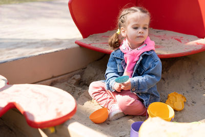Full length of cute girl playing while sitting on sand