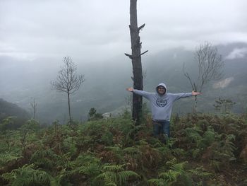 Man with arms outstretched standing on landscape against sky