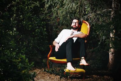 Portrait of young man sitting on chair by trees